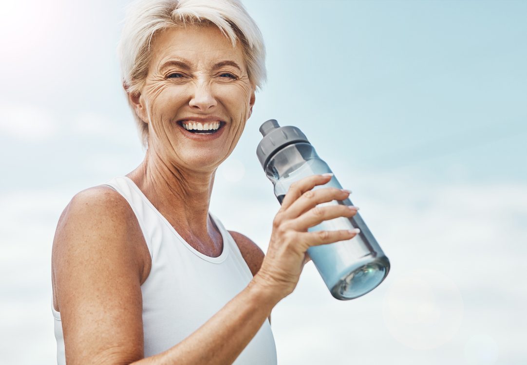 Senior woman, fitness and water bottle with smile for hydration or thirst after workout, exercise or training in nature. Portrait of happy elderly female smiling for natural refreshment on mockup